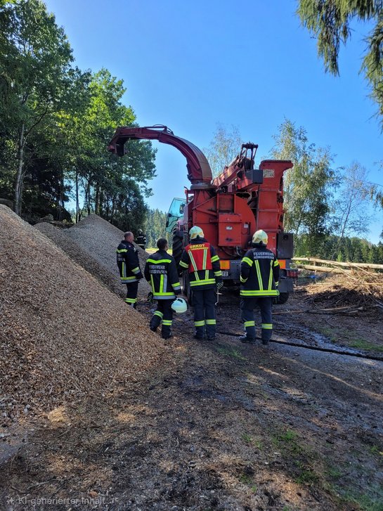 Feuerwehrleute bei Holzhacker in Oberösterreich neben Holzschnitzelberg